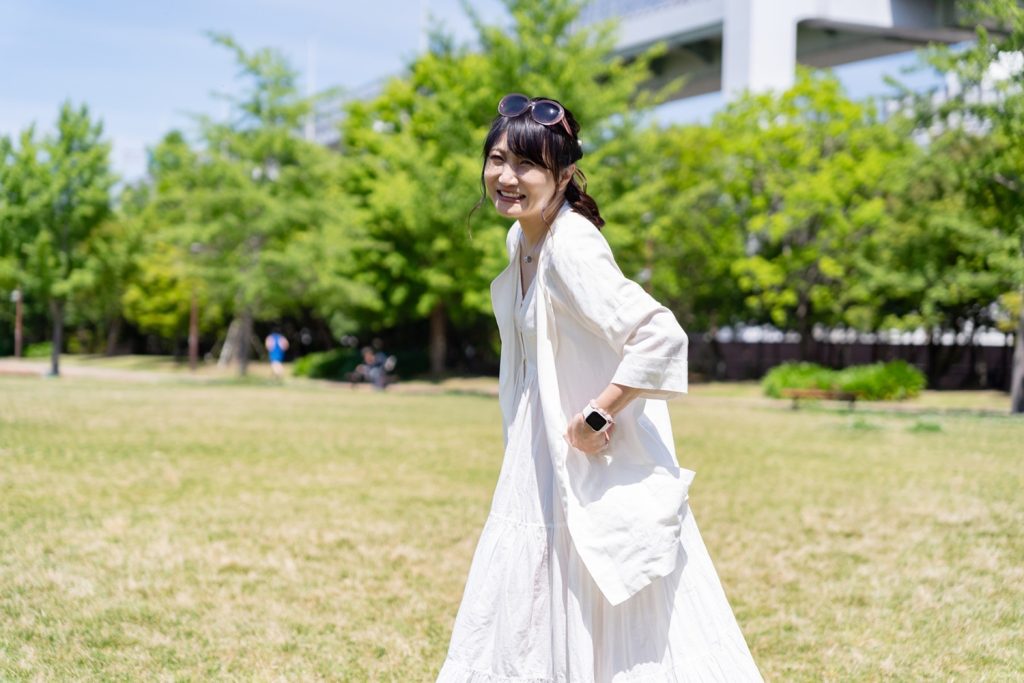 白いワンピースで笑顔のアパレルモデルが公園を歩く